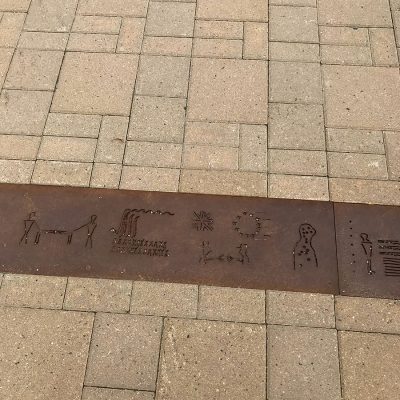 Metal strip on ground with etched in figures. The strip is between interlocking stones.